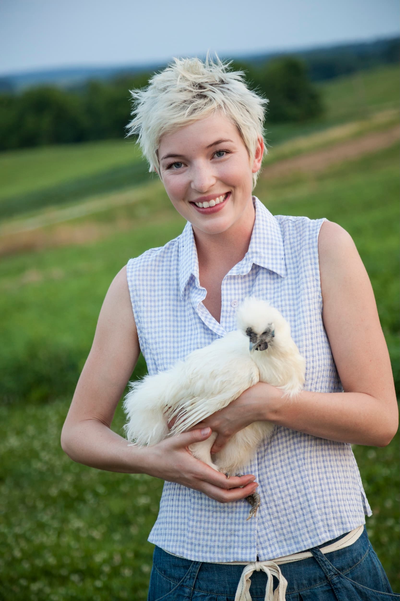 Une éleveuse souriante porte une poule Soie blanche